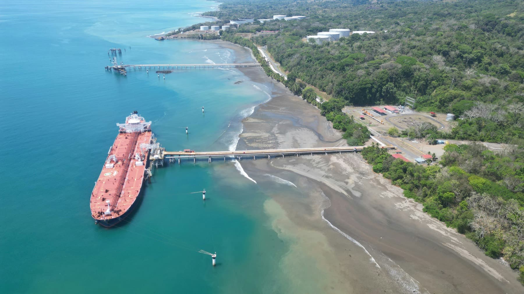 Crude tanker berthed at a coastal terminal jetty with storage tanks onshore